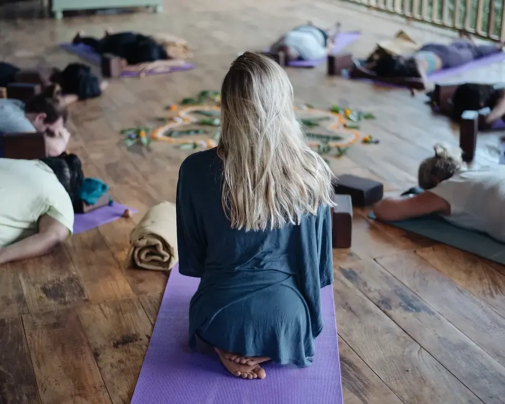 An instructor kneeling on her mat during a group class on the shala